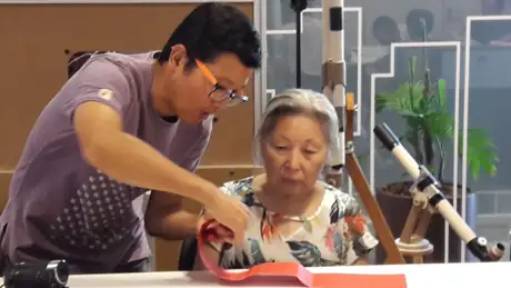 Marcio Okabe ensinando origami a uma senhora no Sesc Paulista